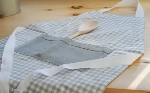 Gotowy fartuch kuchenny w kratkę, z drewnianą łyżką w kieszeni. Idealny poradnik, jak uszyć fartuch kuchenny.