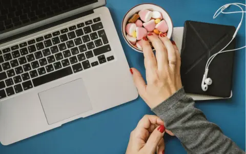 Eine Hand greift nach Süßigkeiten neben einem Laptop. Das Bild symbolisiert assoziatives Lernen: Belohnung und Fokus.