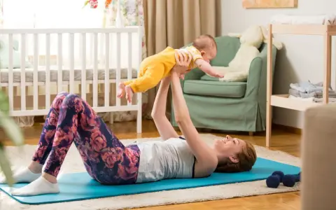 Frau macht Beckenbodentraining mit Baby. Sie liegt auf einer Matte und hebt ihr Kind hoch.