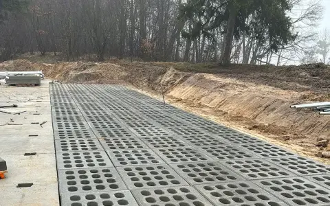 Trwa utwardzenie terenu. Betonowe płyty z otworami tworzą nawierzchnię obok placu budowy z materiałami.