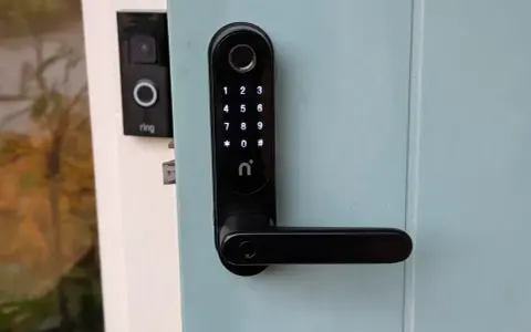Nimly Touch Pro test: Svart digital dörrlås med kodpanel och fingeravtrycksläsare monterat på en ljusblå dörr. Bredvid syns en Ring-ringklocka.