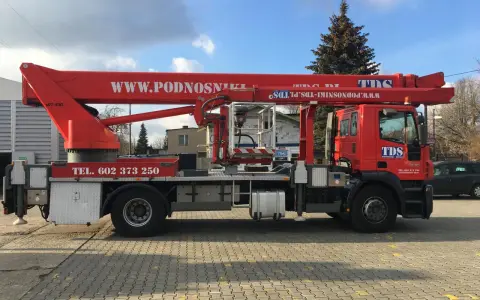 Czerwony podnośnik koszowy WUMAG WT 450 z koszem roboczym i wysięgnikiem. Na pojeździe widnieje napis WWW.PODNOSNIKI-TDS.PL.
