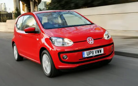 Czerwony Volkswagen up! pędzi po miejskiej drodze, odbijając światła miasta w swojej lśniącej karoserii.