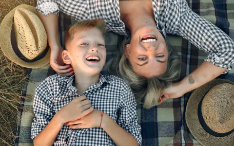 Uśmiechnięta mama i syn leżą na kocu. Idealny dzień na życzenia z okazji Dnia Mamy.
