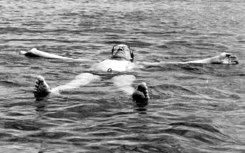Tage Erlander, statsminister, flyter avslappnat på rygg i vattnet, med armarna utsträckta.
