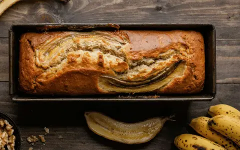 Un delizioso banana bread light appena sfornato, con banane caramellate in superficie, su un tagliere di legno.