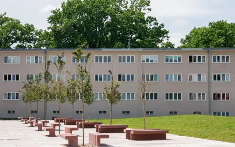 Nowoczesny budynek mieszkalny w stylu wuwa Wrocław z rzędem drzew i betonowych ławek przed fasadą.
