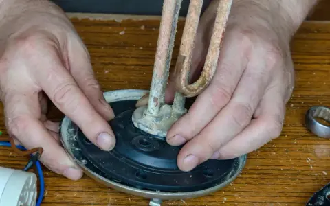 Mains de l'homme ajustant un élément chauffant entartré sur un joint plat, prêt pour le remplacement.