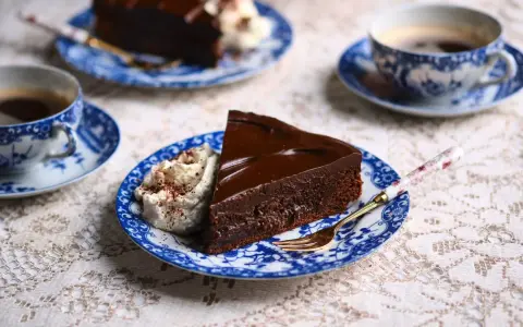 En bit chokladkaka med glansig ganache och vispgrädde, serverad med kaffe. Perfekt för ett enkelt ganache recept.