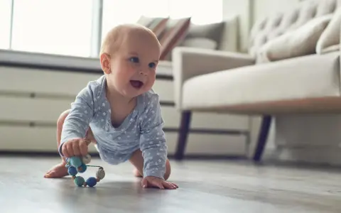 Ein Baby in blauem Sternen-Body krabbelt fröhlich über den Holzboden und greift nach einer bunten Rassel. So erkunden Babys die Welt!
