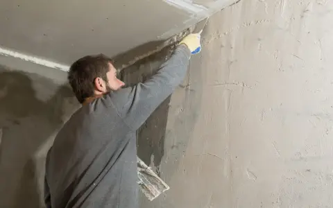 Hombre aplicando masilla en una esquina para quitar el gotele del techo.