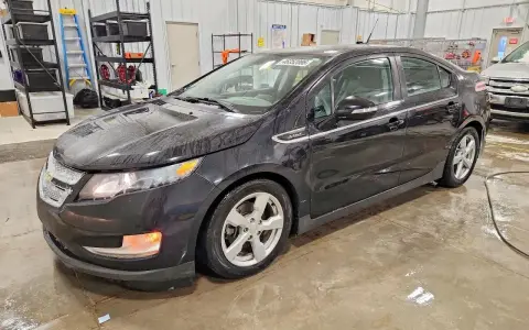 Czarny Chevrolet Volt stoi w garażu, mokry od deszczu. W tle regały z narzędziami i drabina.