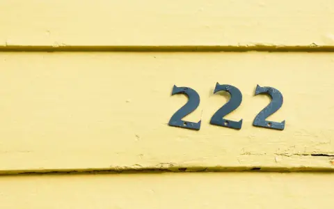 Na żółtej, drewnianej ścianie widnieje anielska liczba 222.