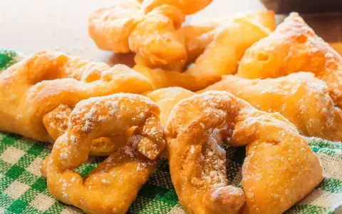 Beignets dorés saupoudrés de sucre glace sur un torchon à carreaux verts.