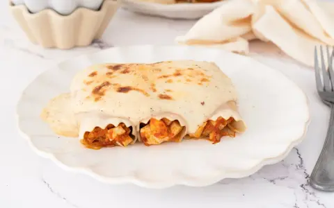 Canelones de atún gratinados con bechamel cremosa, listos para disfrutar en un plato blanco con borde ondulado.