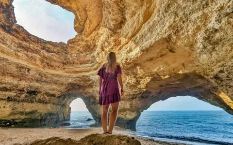 Frau steht in Höhle, blickt auf Meer. Ein Highlight der Algarve.