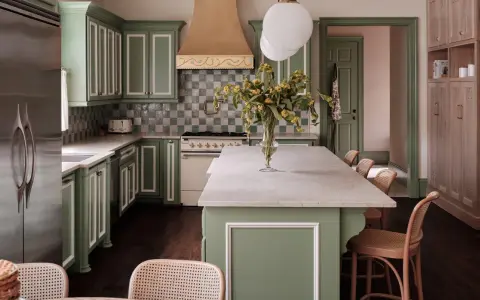 Elegantes cocinas verdes con gabinetes de madera clara, encimeras de mármol y un toque de color en la campana de la estufa.