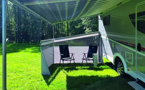 Ett vindskydd från Biltema ger skugga och skydd vid husbilen. Två stolar står redo för avkoppling i gräset.