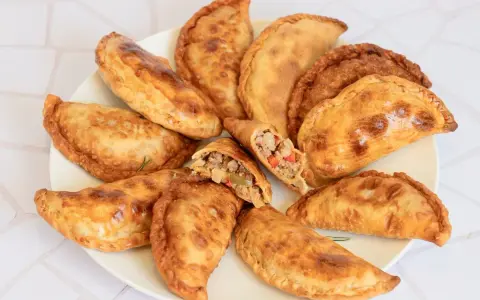 Empanadas de carne doradas y crujientes en un plato, una partida muestra el relleno.