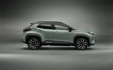 Nowy, zielony toyota crossover Yaris Cross z czarnym dachem i felgami stoi na szarym tle.