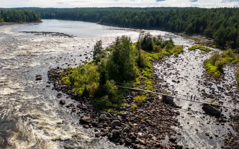 Vattenfall och en träbro över en stenig flod i Kalix, Sverige. Två personer går över bron.