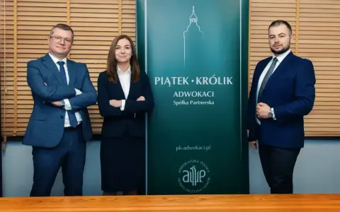 Trzy osoby w garniturach stoją przed zielonym banerem kancelarii "Piątek • Królik Adwokaci".