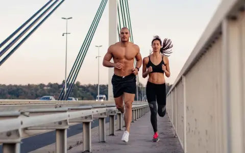 Ein Mann und eine Frau joggen auf einer Brücke. Beide haben sichtbare bauchmuskeln, ein Zeichen für ihr intensives Training.