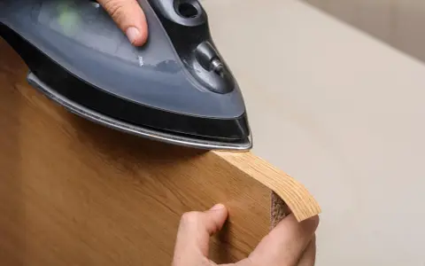 Persona aplica cinta de cantear a un borde de madera con una plancha.