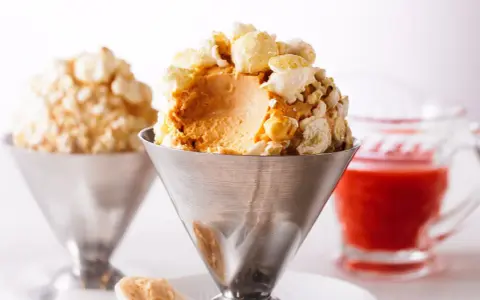 Cremiges Karamell-Popcorn-Eis in einem Metallbecher, garniert mit knusprigem Popcorn. Ein süßer Genuss!