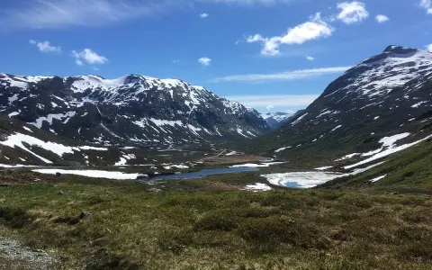 Vacker dalgång med snöklädda berg, en sjö och grönskande sluttningar. En väg slingrar sig fram, kanske en del av trollväggen.