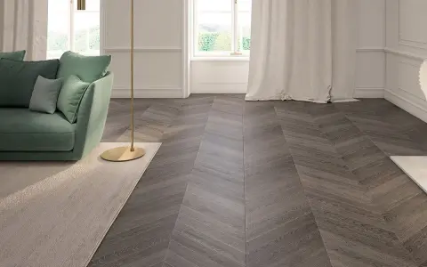 Elegante soggiorno con divano verde, lampada dorata e un tappeto beige. Il pavimento in parquet a spina di pesce, con un colore scuro e venature evidenti, completa l'arredamento.