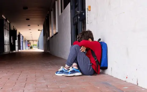 Ein Junge sitzt traurig in einem Schulflur, den Kopf in den Armen vergraben. Er fühlt sich allein, als ob mein Kind gemobbt wird und der Lehrer nichts tut.