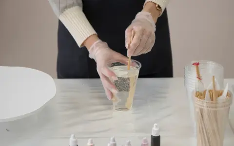 Hände mit Handschuhen mischen zwei komponenten harz in einem Becher. Kleine Farbtropfflaschen stehen bereit.