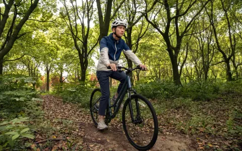 Mężczyzna w kasku jedzie rowerem trekkingowym po leśnej ścieżce. Taki rower to wszechstronny towarzysz podróży.
