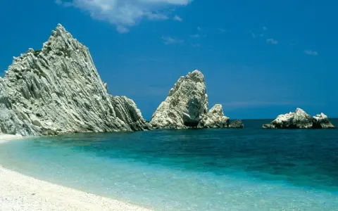 White pebble beach with turquoise water and dramatic white rock formations under a clear blue sky.