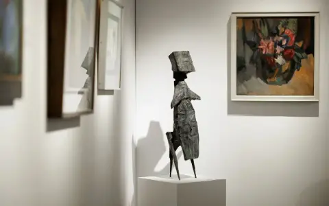 A striking bronze sculpture stands on a pedestal at the London Art Fair, surrounded by framed paintings.
