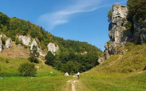 Słoneczna pogoda zachęca do wędrówki po szlakach Doliny Kobylańskiej. Widać rowerzystę i wspinaczy na skale.