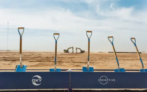 Symboliczne łopaty na placu budowy, gdzie Occidental Petroleum (OXY) rozpoczyna nowy projekt. W tle koparki i wieża.