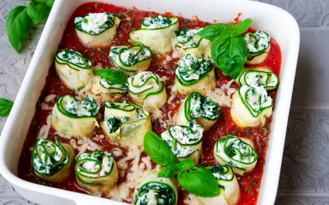 Zucchini-Cannelloni mit Ricotta-Spinat-Füllung in Tomatensauce, garniert mit frischem Basilikum.