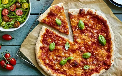 En härlig hemmagjord pizza med tomatsås och ost, toppad med färsk basilika. Bredvid en fräsch sallad med gröna bönor och körsbärstomater.
