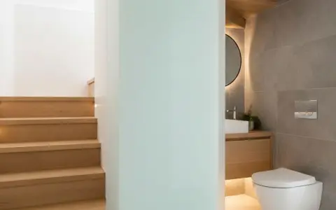 Escaliers en bois menant à un wc sous pente moderne, avec lavabo et miroir rond.