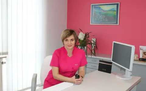 Lekarka w różowym uniformie siedzi przy biurku w gabinecie estetycznym.
