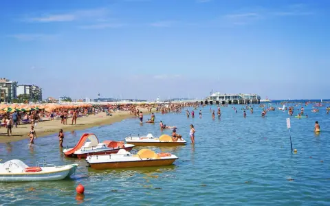 Spiaggia affollata a Gabicce, con ombrelloni colorati, gente in acqua e pedalò. Un'estate vivace al banana beach Gabicce.