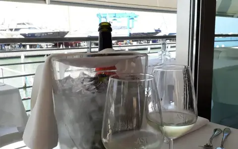 Un bicchiere di vino bianco e una bottiglia in un secchiello di ghiaccio, con vista sul porto e yacht, al ristorante club nautico Rimini.