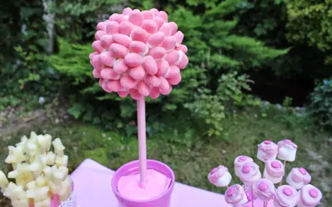 Un árbol de gominolas rosa, decorado con dulces, preside una mesa de fiesta al aire libre.