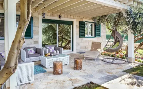 Przytulny taras z przedłużeniem dachu nad tarasem, rattanowe meble, wiszący fotel i kamienna posadzka.