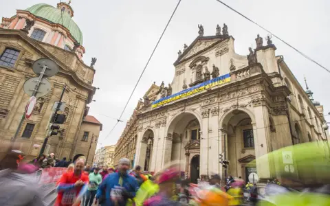Löpare i Prag halvmarathon passerar en byggnad med en banderoll "HANDS OFF UKRAINE, PUTIN!".