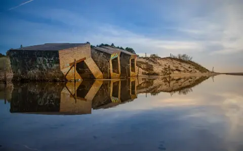 Zniszczone bunkry w Darłówku, z graffiti na ścianach, odbijają się w spokojnej wodzie.