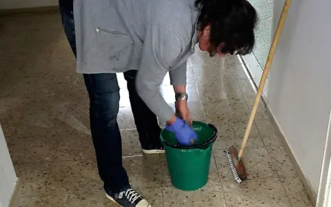 Sprzątaczka w szkole, w niebieskich rękawiczkach, przygotowuje się do pracy. Zastanawiasz się, ile zarabia sprzątaczka w szkole?