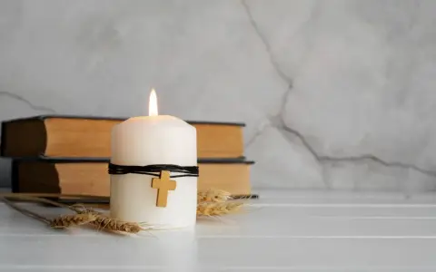 Płonąca świeca z krzyżykiem, obok starych ksiąg i kłosów zbóż. Symbol nadziei i wiary, jak piękna kolęda.